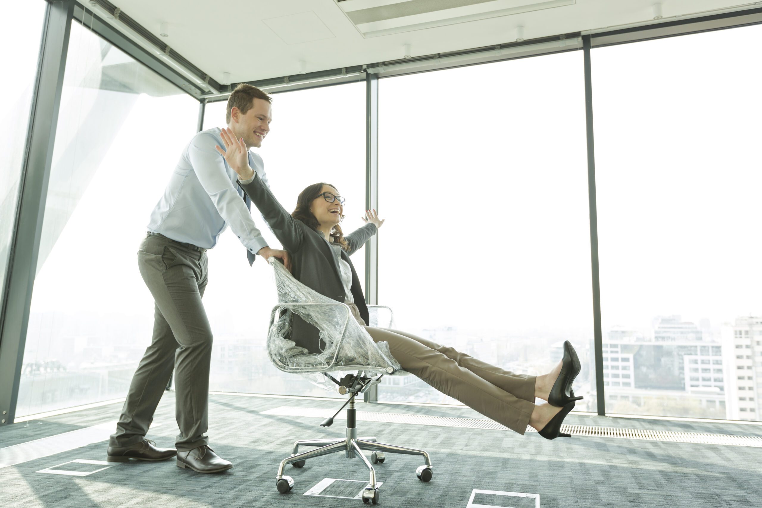 Businessman pushing businesswoman in office chair